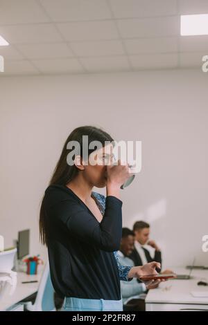 Nahaufnahme einer braunen Geschäftsfrau, die Kaffee aus ihrer grünen Tasse trinkt, während sie im Büro steht Stockfoto