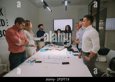 Große Unternehmensgruppe diskutiert über die Geschäftspläne, während sie über dem Tisch im CO-Arbeitsbereich steht Stockfoto
