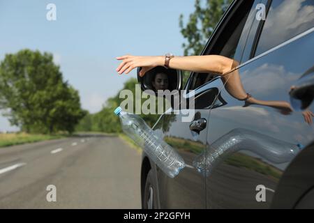 Der Fahrer wirft die Plastikflasche vom Autofenster weg. Müll auf der Straße Stockfoto