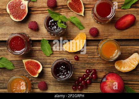 Gläser mit verschiedenen Marmeladen und frischen Zutaten auf Holztisch, flach liegend Stockfoto