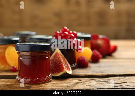 Gläser mit verschiedenen Marmeladen und frischen Zutaten auf Holztisch, Platz für Text Stockfoto