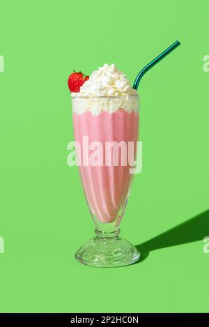 Milchshake mit Erdbeergeschmack in hellem Licht, minimalistisch auf einem grünen Tisch. Köstlicher hausgemachter Milchshake mit Vanilleeis und Erdbeeren Stockfoto