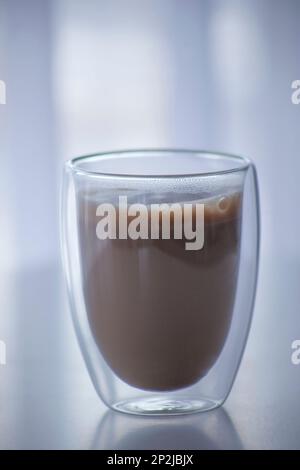 Kaffee mit Milch in einem transparenten Glas mit doppeltem Boden. Ein beliebtes Getränk in einem Originalglas Stockfoto