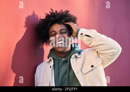 Ein fröhlicher afroamerikanischer Kerl, der über die rote Wand lacht, Porträt. Stockfoto