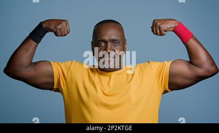 Porträt reifer, afrikanischer Sportler, der sich im grauen Studiohintergrund posiert starker, muskulär sportlicher männlicher Sportler, zeigt Bizeps aufgeblasen Stockfoto