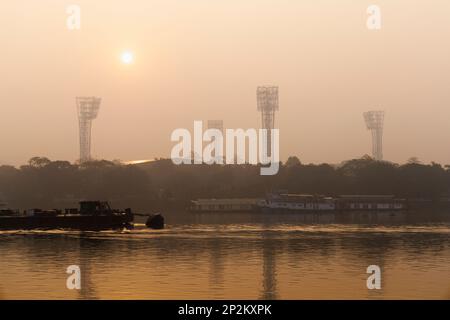 Sonnenaufgang in der rauchigen Atmosphäre über dem Hooghly River am Eden Gardens Cricket-Stadion in Kalkutta, der Hauptstadt von Westbengalen, Indien Stockfoto