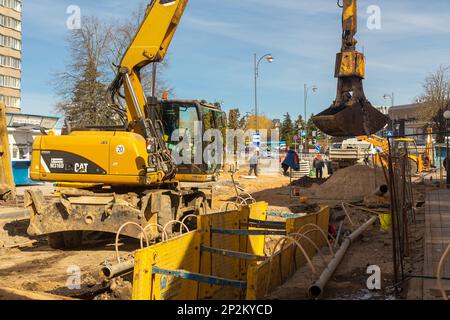 Grodno, Weißrussland - 06. März 2022: Hydraulikbagger füllt Tiefaushub und wird während der Installation des Abflussrohrs von einem Grabenkasten mit Erbsenschieferkies unterstützt Stockfoto