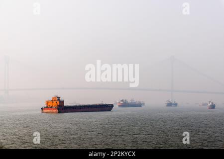 Boote an der Howrah Bridge in frühmorgendlicher Smoggy Atmosphäre über dem Hooghly River in Kalkutta, der Hauptstadt von Westbengalen, Indien Stockfoto