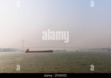 Boote an der Howrah Bridge in frühmorgendlicher Smoggy Atmosphäre über dem Hooghly River in Kalkutta, der Hauptstadt von Westbengalen, Indien Stockfoto