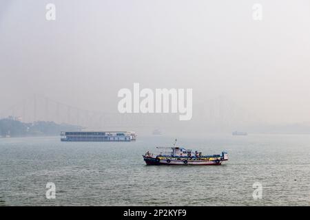 Boote an der Howrah Bridge in frühmorgendlicher Smoggy Atmosphäre über dem Hooghly River in Kalkutta, der Hauptstadt von Westbengalen, Indien Stockfoto