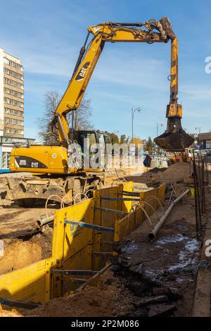 Grodno, Weißrussland - 06. März 2022: Hydraulikbagger füllt Tiefaushub und wird während der Installation des Abflussrohrs von einem Grabenkasten mit Erbsenschieferkies unterstützt Stockfoto