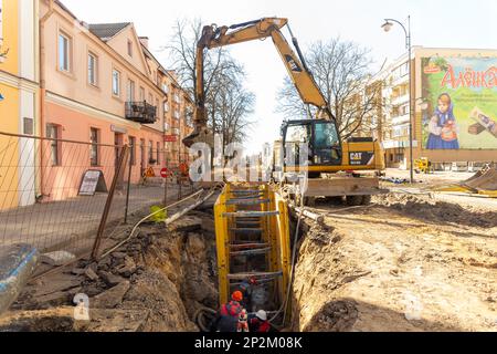 Grodno, Weißrussland - 06. März 2022: Hydraulikbagger füllt Tiefaushub und wird während der Installation des Abflussrohrs von einem Grabenkasten mit Erbsenschieferkies unterstützt Stockfoto