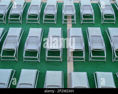 Zusammengeklappte Sonnenliegen in Reihen auf einem grünen Deck an Bord eines Kreuzfahrtschiffes Stockfoto