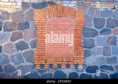 Mauerwerk aus Stein mit versteinerten Fenstern mit roten Ziegeln. Stockfoto