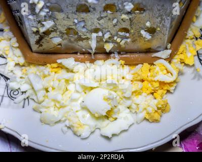 Geriebenes Ei, Eiweiß. Eiweißprodukt. Salatzubereitung. Geriebenes gekochtes Ei auf einem Küchenbrett. Stockfoto