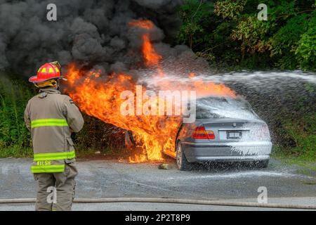 Saint John, NB, Kanada - 18. August 2022: Ein geparktes Auto, das in Flammen stand. Ein Schaum mit Wasser bekämpft das Feuer, während ein Feuerwehrmann zusieht. Stockfoto