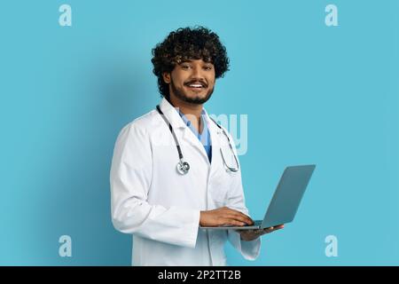 Fröhlicher hindu-Doc mit Laptop, isoliert auf blau Stockfoto