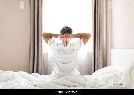 Gut ausgeruhter Mann mittleren Alters, der zu Hause im Bett sitzt Stockfoto