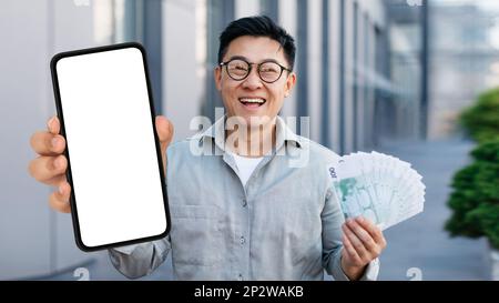 Happy Asian Man Mit Leerem Smartphone Und Bargeld Im Freien Stockfoto