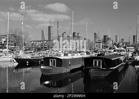 Hausboote und Yachten in South Dock, Rotherhithe, London Docklands, Großbritannien, mit Canary Wharf im Hintergrund Stockfoto