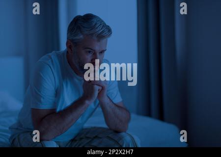 Gestresster erwachsener Mann, der nachts im Bett sitzt Stockfoto