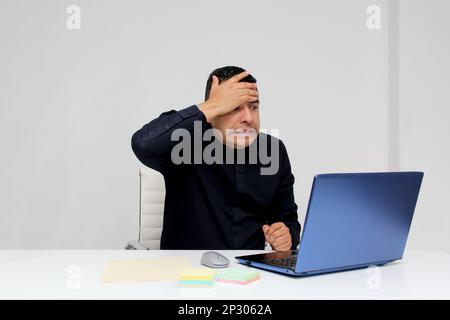 Ein erwachsener Latino-Mann arbeitet von seinem Offie aus mit seinem Laptop wegen Überarbeit, leidet unter Stress, Verzweiflung, Wut, physischer und metallischer Erschöpfung, Burnout Stockfoto