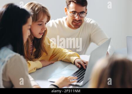 Junge Mädchen, die an einem Computerkurs teilnehmen, mit einem Lehrer, der sie in einer Programmierstunde führt. Männlicher Erzieher, der digitale Bildung und eine starke Entdeckung anbietet Stockfoto