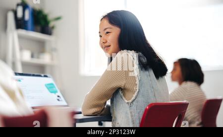 Ein junges asiatisches Mädchen, das in einem Programmierkurs sitzt, mit einem Laptop vor sich und einem starken Interesse im Gesicht. Sie will ihre Programmierfähigkeiten beherrschen Stockfoto