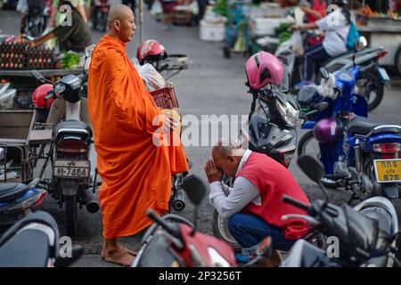 Ein Motorrad Taxi driver in den wichtigsten Markt in der Stadt Phuket, Thailand, Bögen zu einem buddhistischen Mönch und zahlt seinen Respekt mit einer traditionellen thailändischen 'Wai' Stockfoto