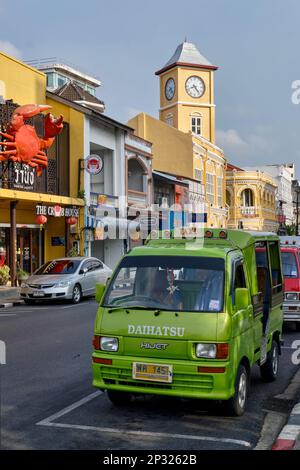 Ein malerischer blau-gelber Songthaew, ein einheimischer Bustyp, vorbei am Wahrzeichen Uhrturm in der Altstadt von Phuket Stadt (Phuket Stadt), Thailand Stockfoto