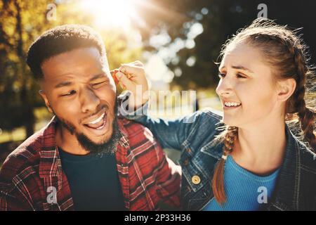 Verspielt, Park und ein Mädchen, das im Sommer ihrem Freund aus Liebe das Ohr zieht, während er ein Date hat. Paare, Spiele oder Natur mit einem jungen Mann und Stockfoto