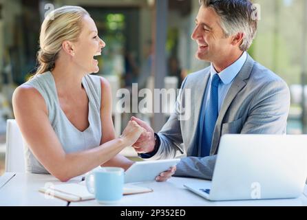 Es ist immer ein Vergnügen, Geschäfte zu machen. Zwei reife Geschäftsleute, die sich die Hand schütteln, während sie an einem Tisch sitzen. Stockfoto