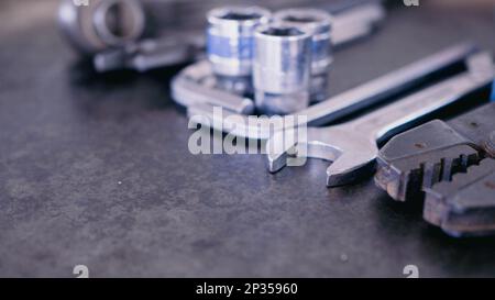 Handwerkzeuge bestehend aus Schraubenschlüsseln, Zangen, Steckschlüsseln, auf altem Stahlblechhintergrund angeordnet. Stockfoto