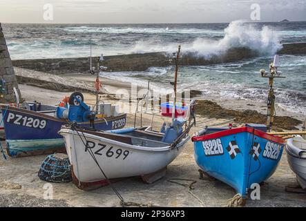 Fischerboote in einem Küstendorf, mit Wellen, die über Wellenbrecher stürzen, Sennen Cove, Sennen, Cornwall, England, Vereinigtes Königreich Stockfoto