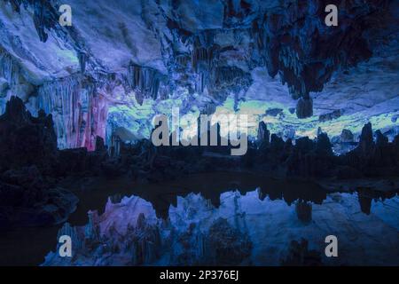 Das Innere einer Kalksteinhöhle mit Stalaktiten und Stalagmiten, die in einem Teich reflektiert werden, erleuchtet mit künstlichem Licht, Schilfrohrflötenhöhle, Guilin Stockfoto
