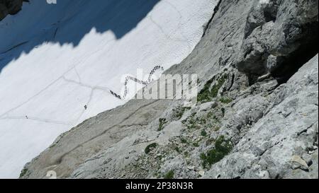 Blick von oben auf Menschen, die auf dem Zickzack-Gletscher spazieren. Große Schlange, Stau. Zugspitze-Massiv in den bayerischen alpen Stockfoto