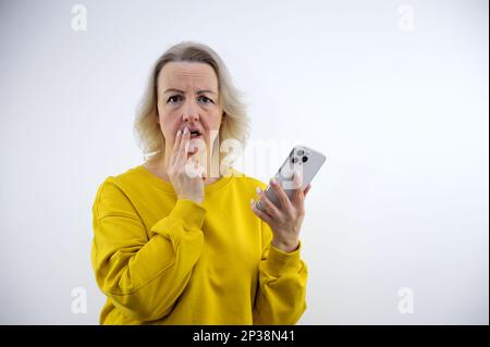 Ängstliche Erfahrung eine Erwachsene Frau mit Handy in der Hand hält zwei Finger an ihre Lippen und denkt an Unerwartetes, unangenehme Empfindungen und negative Emotionen, alarmiert das Telefon Stockfoto