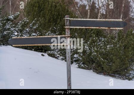 Rostiges, rostiges Hinweisschild im Winter, das in zwei Richtungen zeigt. Stockfoto