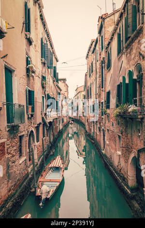 Alter schmaler Kanal in Venedig mit grünem Wasser, mittelalterliche Häuser an den Seiten und Boote (alter Fotoeffekt) Stockfoto