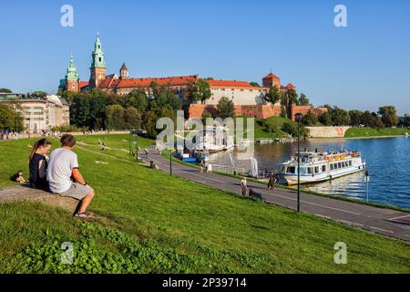 Stadt Kraków (Krakau) in Polen genießen die Menschen den Blick auf das Wawelschloss am Fluss Wisła mit Tourbooten entlang der Flusspromenade. Stockfoto