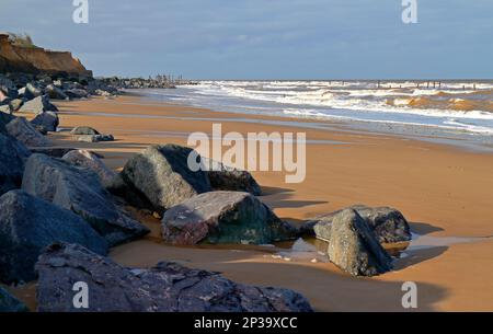 Blick auf den Strand im Winter mit importierten Felsabwehren und verlassenen Holzbauern an der Norfolkküste in Happisburgh, Norfolk, England, Großbritannien. Stockfoto