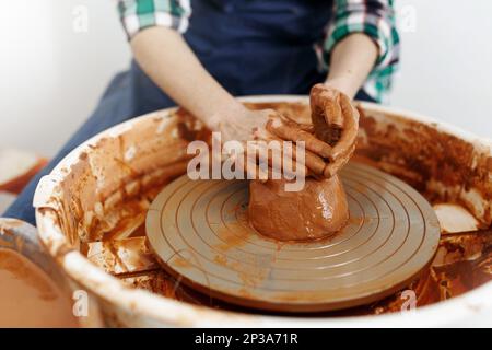 Zugeschnittenes Bild eines unbekannten weiblichen Keramikmachers, der mit dem Keramikrad in Cozy Workshop arbeitet, bildet eine zukünftige Vase oder Tasse, kreative Menschen Stockfoto