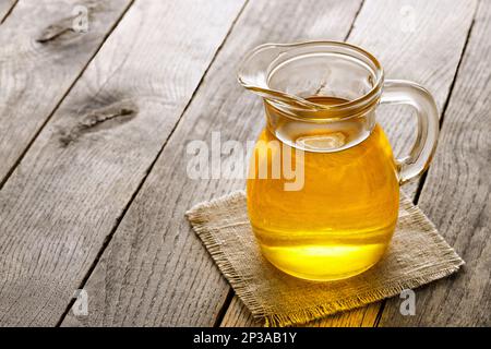 Speiseöl in Glaskanne auf Holztisch Stockfoto