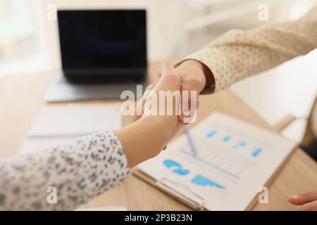 Nahaufnahme von Managern, die sich am Bürotisch die Hand schütteln. Stockfoto