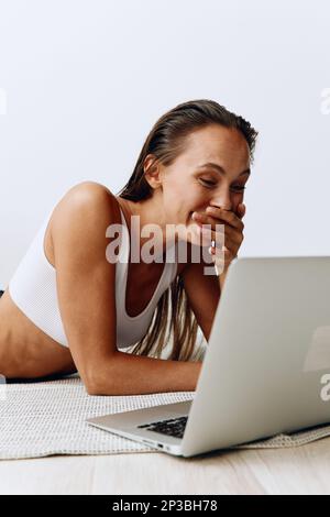 Frau, die zu Hause mit einem Freiberufler arbeitet, der zu Hause mit einem Laptop arbeitet und online auf dem Boden liegt und mit Zähnen lächelt Stockfoto