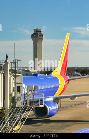 Austin, Texas - Februar 2023: Heckflosse eines Passagierflugzeugs der Boeing 737 von Southwest Airlines am Terminal mit dem Flugverkehrskontrollturm des Flughafens Stockfoto