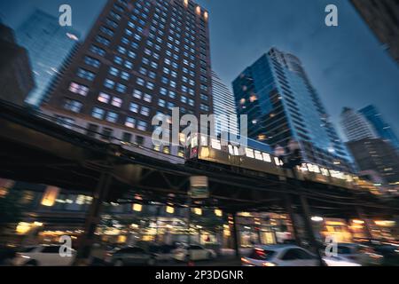 Hochbahn in Chicago. Zug der öffentlichen Verkehrsmittel in unscharfer Bewegung gegen Wolkenkratzer in Downtown Disctrict bei Nacht. Stockfoto