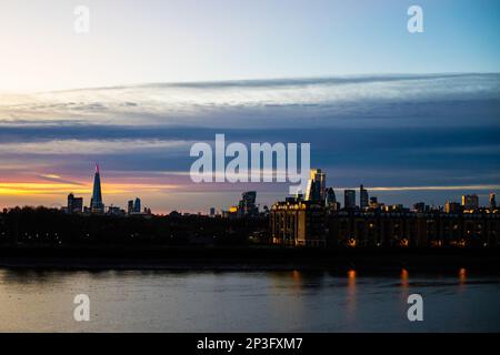 Sonnenuntergang über der Stadt London und der Themse an einem ruhigen Tag. Die untergehende Sonne strahlt in der Dämmerung ein wunderschönes Licht auf die Gebäude. Stockfoto