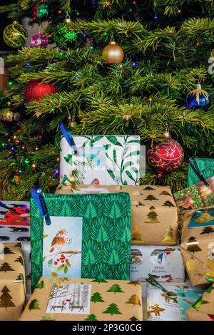 Ein Haufen verpackter Weihnachtsgeschenke liegt unter dem Weihnachtsbaum. Sie sind in verschiedene gemusterte Geschenkpapiere eingewickelt und mit Geschenkanhängern versehen. Stockfoto