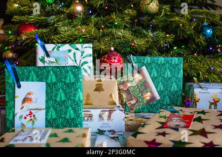 Ein Haufen verpackter Weihnachtsgeschenke liegt unter dem Weihnachtsbaum. Sie sind in verschiedene gemusterte Geschenkpapiere eingewickelt und mit Geschenkanhängern versehen. Stockfoto